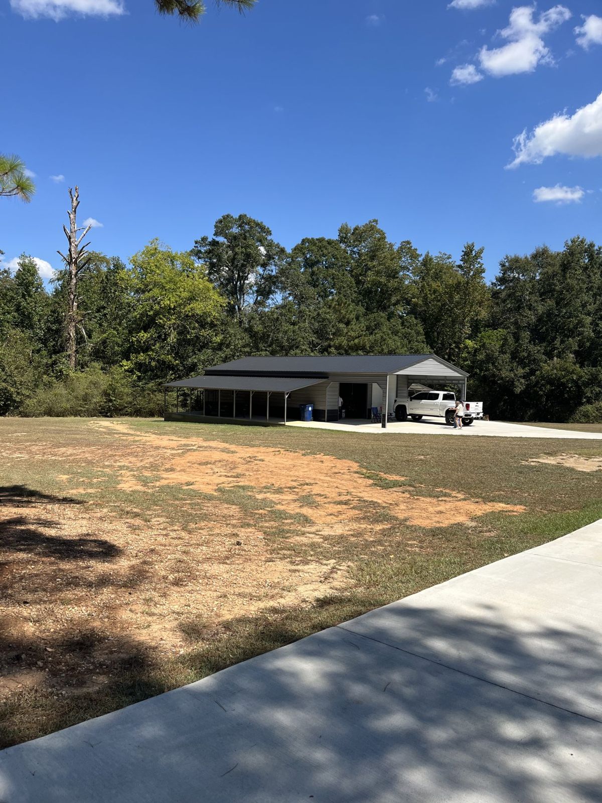 Detached metal shop with lean-to covers and new concrete; bare soil from recent grading